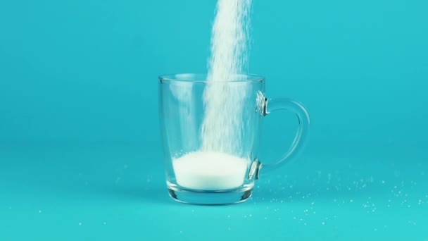 Ρίξτε ζάχαρη κούπα γυαλί παχύ κάτω μπλε αντίθεση φόντο αργή κίνηση - Πλάνα, βίντεο