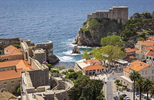 View from the fortress Dubrovnik on parts of the medieval city and the Mediterranean Sea. One can walk around on the ramparts the city. This make a lot of tourists. This one has many interesting views on the roofs of old houses. Tourists are enjoying - Photo, Image
