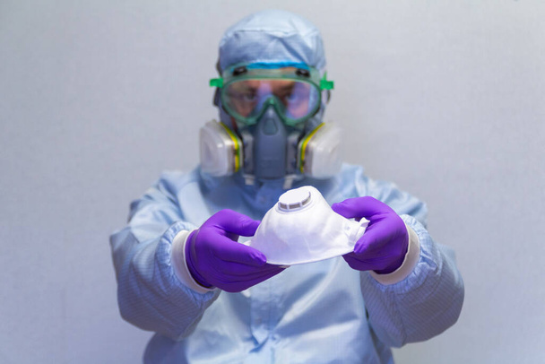 Ένας άνδρας με προστατευτική στολή επιδεικνύει και προσφέρει μια ιατρική μάσκα για προσωπική προστασία από ιούς - έννοια της υγείας και της ιατρικής, συμβουλές πρόληψης - Φωτογραφία, εικόνα