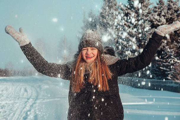 Молодая девушка-подросток покрывает себя снегом и смеется в восторге. Веселье и радость зимой на открытом воздухе. Зимние каникулы в деревне
. - Фото, изображение