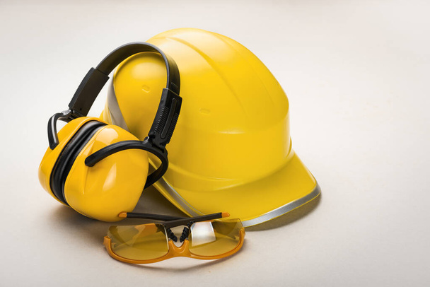 Casque jaune et écouteurs avec lunettes sur fond clair : concept d'équipement personnel de santé et de sécurité
. - Photo, image