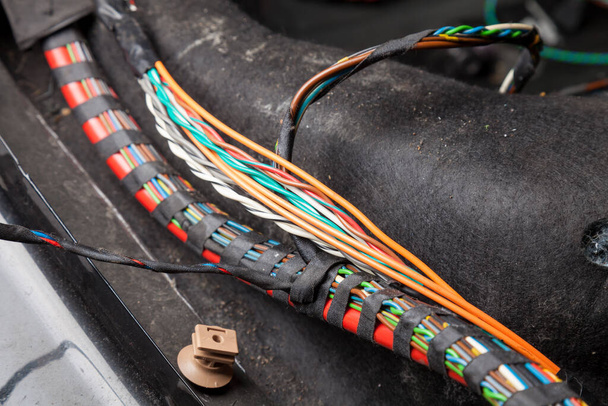 Velký široký kabel s pestrobarevnými oranžovými a zelenými dráty, konektory a svorkami v opravně kabelů a elektrikáři pro připojení a přenos elektřiny a digitálního signálu v autě - Fotografie, Obrázek