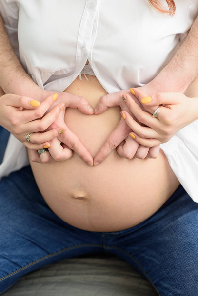 Future father shows fingers heart on the belly of his pregnant wife - Foto, afbeelding