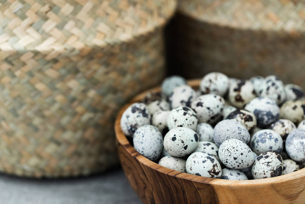 Wooden bowl with heap of small quail eggs on kitchen. Wicker straw basket on background. Empty place for text. - Photo, Image