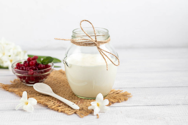 Homemade yogurt in a glass jar on a wooden light background with a ceramic spoon. Healthy diet food. Vegetarian food. Copy space - Zdjęcie, obraz