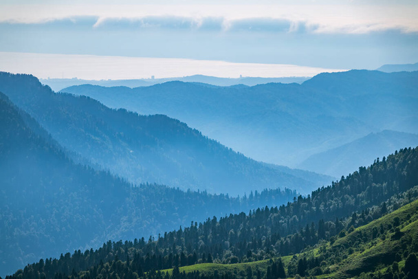 Вид на Зелёную долину, окруженную высокими горами на летнем закате. Слои гор в тумане во время заката. Многослойные туманные существительные. Красная Поляна, Сочи, Россия
. - Фото, изображение