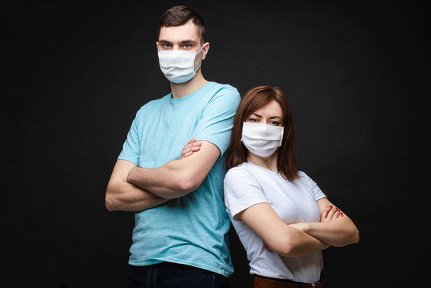 Young couple wearing protective masks. Stock photo portrait of a young Caucasian couple in aseptic sterile masks looking at camera with folded arms. - Fotografie, Obrázek