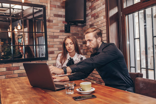 Üzleti pár, akik munkáról beszélgetnek, miközben a kávézóban ülnek és laptopot használnak. Az üzletember elmagyarázza az ötleteit a női partnerének.. - Fotó, kép