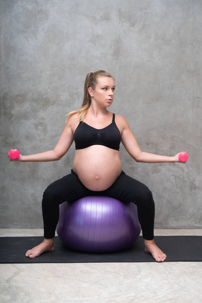Portrait of pretty pregnant woman exercises with fitball and dumbbells in the gym. Working out and fitness, pregnancy concept - Photo, Image