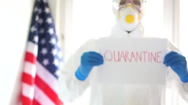 Close portrait of a doctor man in a protective suit holding a sign saying quarantine. Quarantine and self-isolation. Covid19 coronavirus epidemic in the USA - Záběry, video