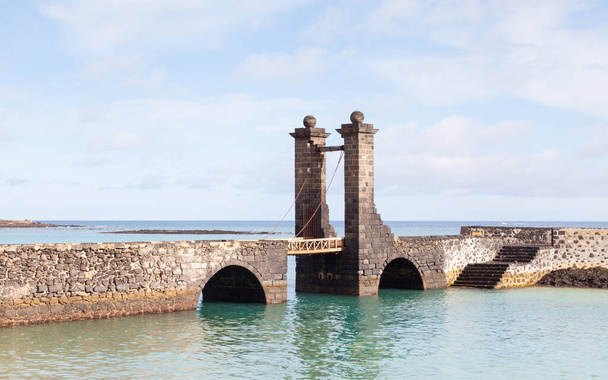 Мост Яйц. Пуэнте-де-лас-Болас ведет к замку Сан-Габриэль в портовом городе Арресифе на испанском острове Льяроте
. - Фото, изображение