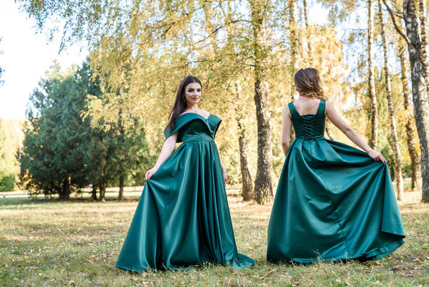 Panie w eleganckich zielonych sukienkach spacerujące w jesiennym parku. Brunetka dziewczyna Dreamy młode dziewczyny śmieją się na świeżym powietrzu - Zdjęcie, obraz
