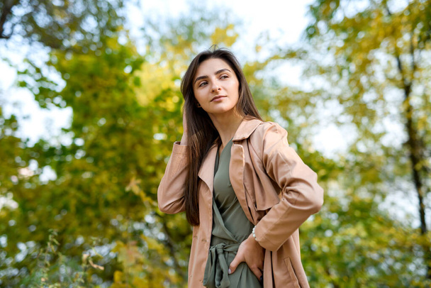 Portrait of brunette woman in green dress posing in autumn park - Фото, зображення