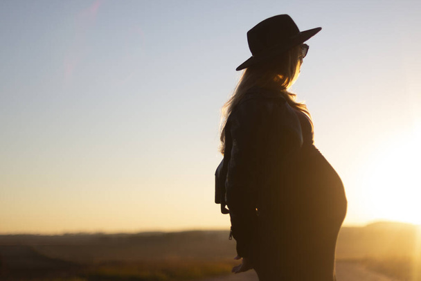 Beautiful pregnant woman in hat, sunglasses looking to sunset outdoors. Travel - Fotoğraf, Görsel
