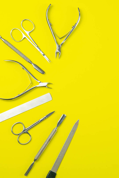 A set of cosmetic tools for manicure and pedicure. Manicure scissors, cutters, nail clippers stand on a yellow background. Top views with clear space. - Photo, Image