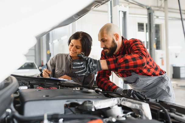 Male and female mechanics working on car - Фото, изображение