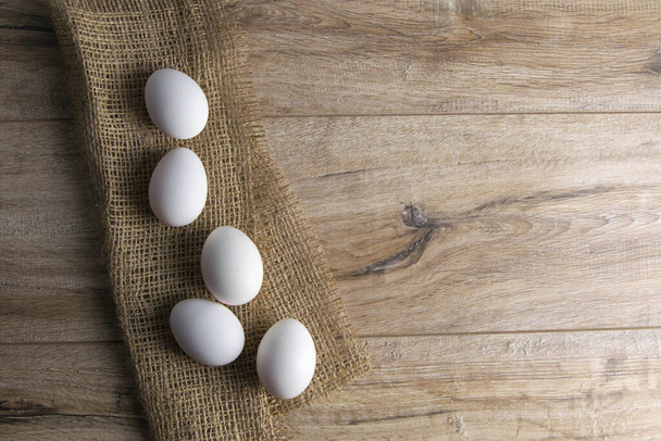 White and quail eggs stand on a burlap on a wooden table. Top views with clear space - Фото, изображение