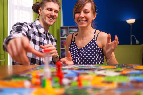 Board game concept- friends spend time together. Board game field, figures, dice, coins and sandglass. Two people holding cards funny play and hug - Photo, Image