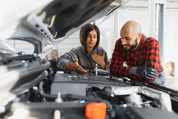 Auto car repair service center. Mechanic examining car engine. Female Mechanic working in her workshop. Auto Service Business Concept. Pro Car female Mechanic Taking Care of Vehicle. - Zdjęcie, obraz