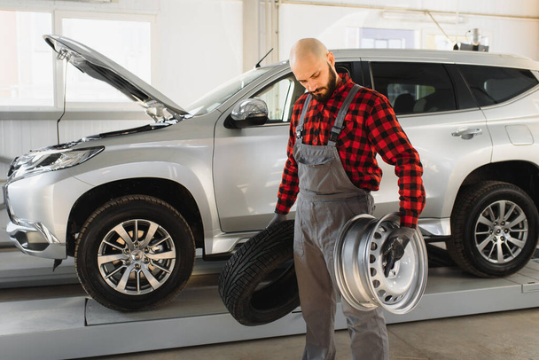 Mechanic holding a tire tire at the repair garage. replacement of winter and summer tires. - Foto, Imagen