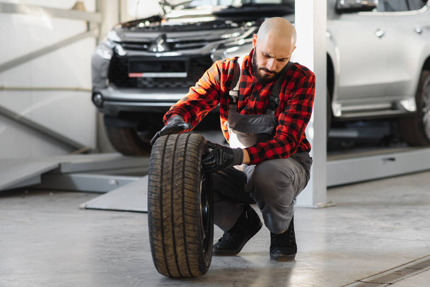 Mecánico sosteniendo un neumático en el garaje de reparación. sustitución de neumáticos de invierno y de verano. - Foto, imagen