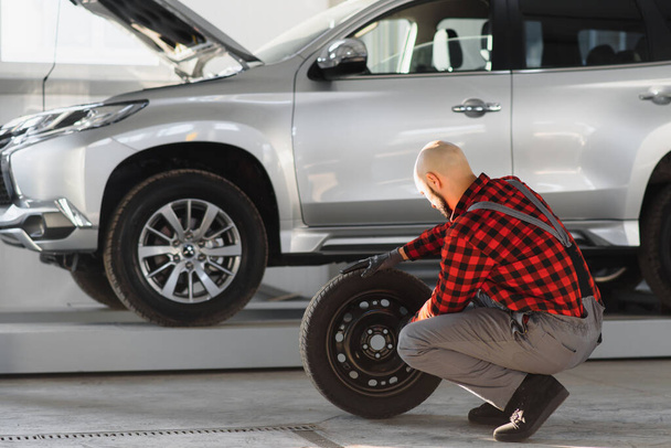 Hombre reparando una rueda de coche en un garaje
 - Foto, Imagen