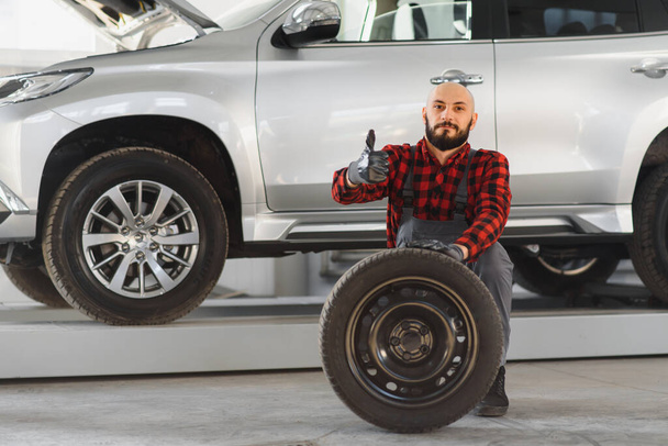 Mécanicien tenant un pneu au garage de réparation. remplacement des pneus d'hiver et d'été. - Photo, image