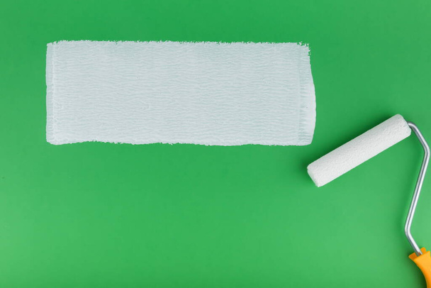 painting roller and strip of white paint on green background - Fotó, kép