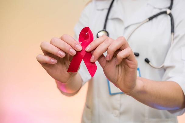Kırmızı kurdele tutan, tıp üniformalı bir kadın doktor. AIDS Günü konsepti - Fotoğraf, Görsel