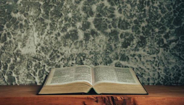 Открыть Библию на старом коричневом деревянном столе. Красивый серый белый фон стены
. - Фото, изображение