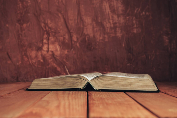 Відкрита Біблія на червоному старому дерев'яному столі. Красивий коричневий фон стіни
. - Фото, зображення