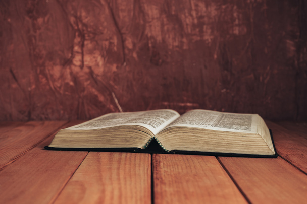 Otwórz Biblię na czerwonym drewnianym stole. Piękne brązowe tło ściany. - Zdjęcie, obraz