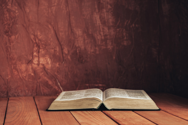 Otwórz Biblię na czerwonym drewnianym stole. Piękne brązowe tło ściany. - Zdjęcie, obraz
