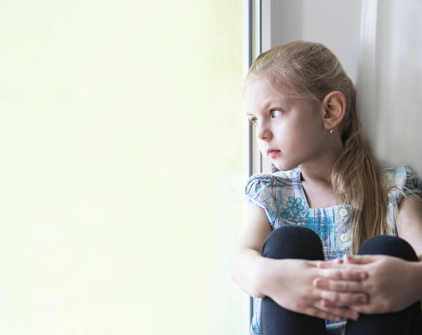Sad child girl  by the window at home. Quarantine. Coronavirus pandemic. Stay home concept.  - Photo, Image