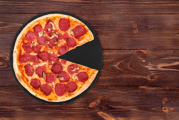 Salami pizza with mushrooms, without slice, on slate bottom, on wooden table, top view space for text - Foto, immagini