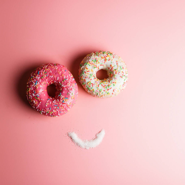 funny smiley of two donuts and banana on a pink background with place for text, an example of junk food - 写真・画像