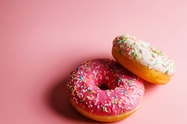 Zwei saftige frische süße Donuts mit Zuckerguss und Streusel auf rosa Hintergrund - Foto, Bild