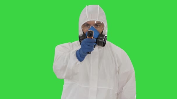 Male doctor in protective suit holding an digital infrared thermometer pointing with it to camera on a Green Screen, Chroma Key. - Video