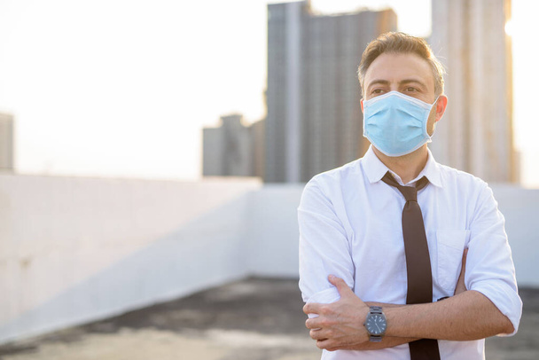 Korona virüsü salgını ve kirlilikten korunmak için maske takan olgun bir işadamı - Fotoğraf, Görsel