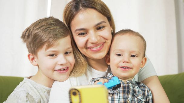 Beautiful mom with sons having a facetime video call. Happy family taking selfies and video chatting at home. Mother's day, unity, connection concept.  - Fotografie, Obrázek