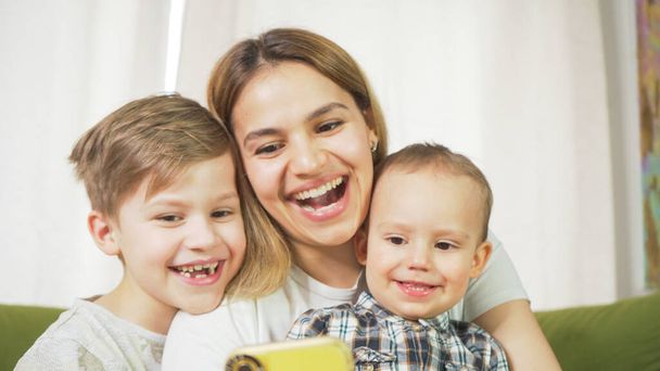 Beautiful mom with sons having a facetime video call. Happy family taking selfies and video chatting at home. Mother's day, unity, connection concept.  - Фото, зображення