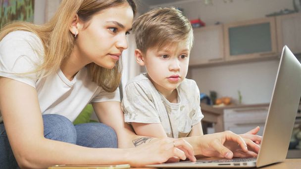 Beautiful mother working from home with her son. Independent focused mom and child studying behind computer.  Home education and work concept. - Φωτογραφία, εικόνα