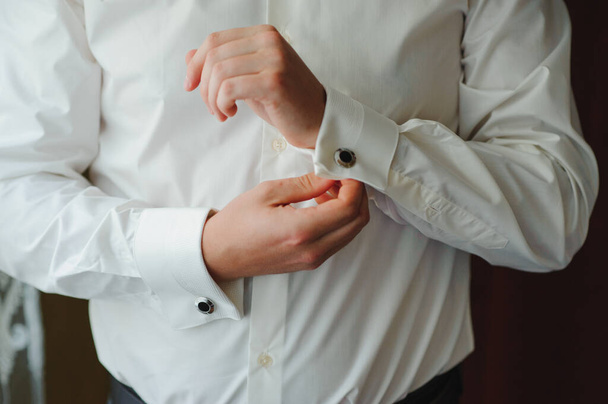 Egy üzletember felöltöztet egy fehér inget közelről, a vőlegény felkészül az esküvői szertartásra. Férfi módra. Ing és gallérbilincs - Fotó, kép