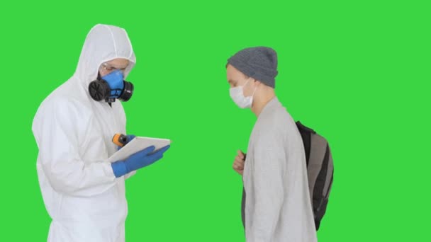 Woman with temperature stoped by medical worker in protective suit who was screening passengers for Covid-19 symptoms on a Green Screen, Chroma Key. - Video, Çekim