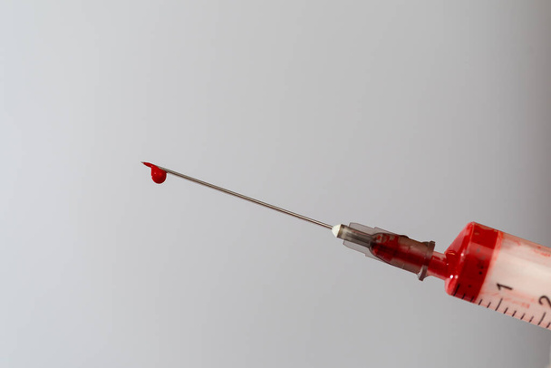 Syringe with a blood sample. A drop of blood at the end of the needle. Blood chemistry. Blood test for viruses. - Fotografie, Obrázek