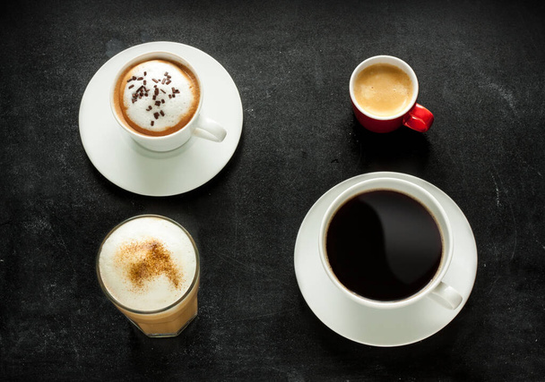 Different kinds of coffee on black chalkboard background. Cappuccino, espresso, americano and latte from above (top view) - cafe menu.  - Zdjęcie, obraz