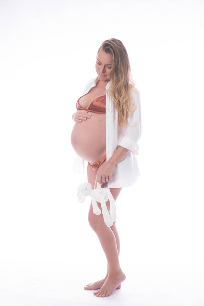 Pretty pregnant woman touching her belly while standing with rabbit toy over white background. Maternity concept - Fotografie, Obrázek