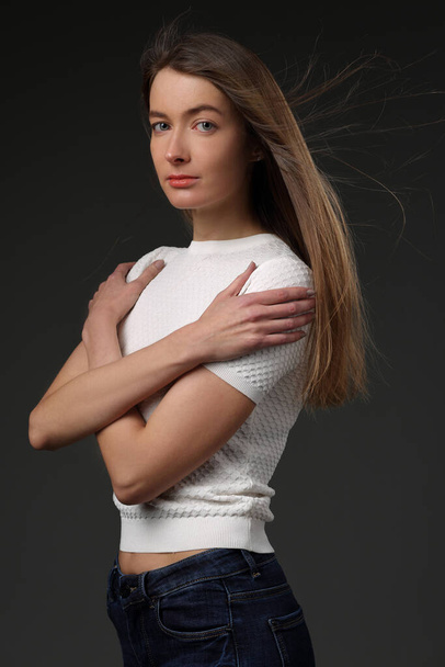 Portrait of a beautiful girl with loose hair in a white t-shirt on a gray background - Fotografie, Obrázek