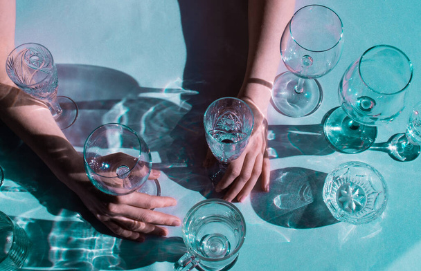 Женские руки с другими бокалами вина на столе на зеленом фоне. Много стаканов для напитков с солнечным светом и тенью
. - Фото, изображение