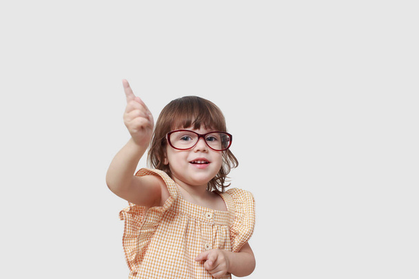 little girl wearing glasses raised her index finger up, she wants to tell us something important to us. Listen carefully to me. Isolated on a grey background. Concept of logical thinking. Copy space - Valokuva, kuva